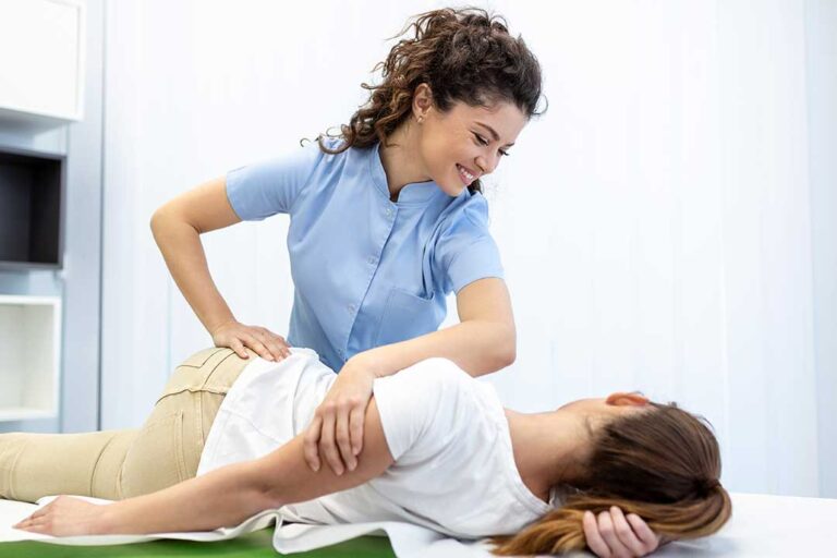 A person gently stretching their neck while seated at a desk with a computer and a pillow nearby.